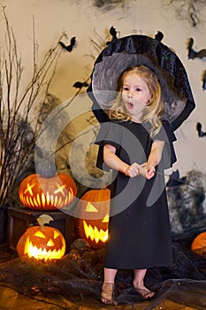 Halloween surprised blonde little witch girl with magic wand. Pumpkins cobwebs.