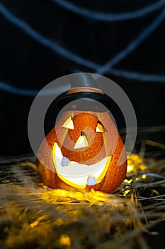 Halloween symbol - glowing Jack o`Lantern pumpkin head with lamp in a pointed black hat in the hay on the background of cobweb