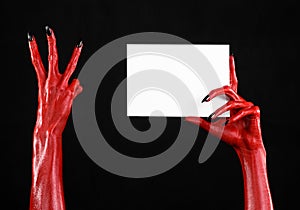 Halloween theme: Red devil hand with black nails holding a blank white card on a black background