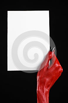 Halloween theme: Red devil hand with black nails holding a blank white card on a black background