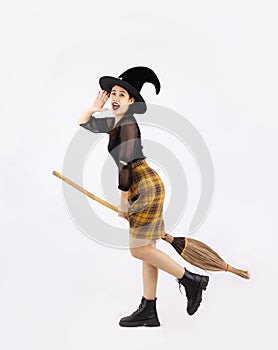 Halloween theme, young pretty asian girl in black dress wearing witch hat and holding broom posing on white background