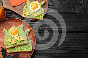 Halloween themed breakfast served on black wooden table, flat lay and space for text. Tasty sandwiches with fried eggs
