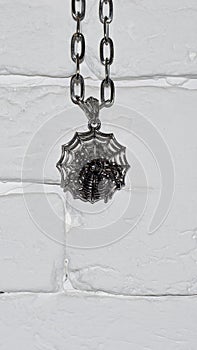 Halloween themed hanging spider hanging on a chain on a white stone wall
