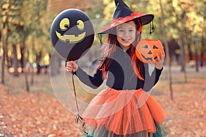 Halloween trick or treat. Portrait smiling girl in witch hat with black balloon . Funny kid in carnival costumes outdoors