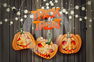 Halloween trick or treat realistic design. Haning pumpkins and lights garland over wooden board background. photo