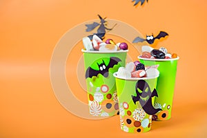 Halloween trick or treat sweets. Paper cups with colourful candies inside and paper silhouettes of bats, ghosts and witch on