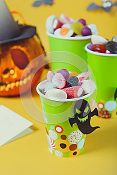 Halloween trick or treat sweets. Paper cups with colourful candies inside and paper silhouettes of bats, ghosts, witch on bright