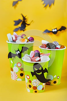 Halloween trick or treat sweets. Paper cups with colourful candies inside and paper silhouettes of bats, ghosts, witch on bright