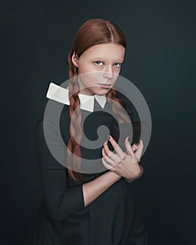 Halloween vampire woman looks directly into the camera holding book. Female portrait in vintage style on dark background.