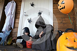 Halloween vibes. Cute child and his father in wizard costumes sitting near house door and looking at how much candy kid collected