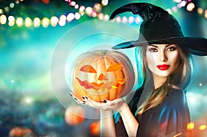 Halloween witch with a carved pumpkin and magic lights in a forest