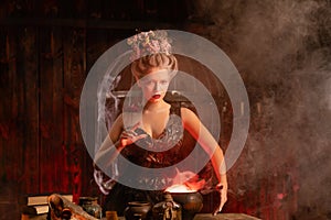 Halloween Witch with cauldron. Beautiful young woman conjuring, making witchcraft photo