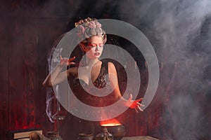 Halloween Witch with cauldron. Beautiful young woman conjuring, making witchcraft photo