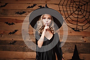 Halloween Witch concept - closeup shot of little caucasian witch child holding index finger at lips, asking to keep