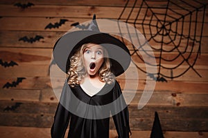 Halloween Witch concept - closeup shot of little caucasian witch child shocking face posing with bat and spider web on wooden stud