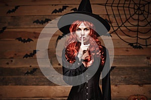 Halloween witch concept - Happy Halloween red hair Witch doing silence gesture with finger on her lips over old wooden