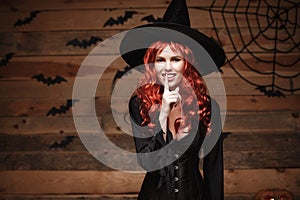 Halloween witch concept - Happy Halloween red hair Witch doing silence gesture with finger on her lips over old wooden studio back