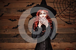 Halloween witch concept - Happy Halloween red hair Witch holding posing with shocked face over old wooden studio background.