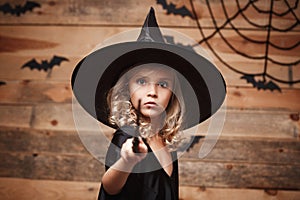 Halloween Witch concept - little witch child enjoy playing with magic wand. over bat and spider web background.