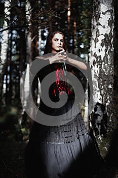 Halloween Witch in a dark forest. Beautiful young woman in witches costume . Halloween art design. Horror Background For Halloween