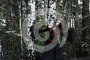 Halloween Witch in a dark forest. Beautiful young woman in witches costume . Halloween art design. Horror Background For Halloween