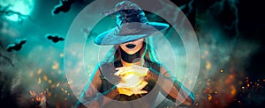 Halloween Witch girl with making witchcraft, magic in her hands, spells. Beautiful young woman in witches hat conjuring