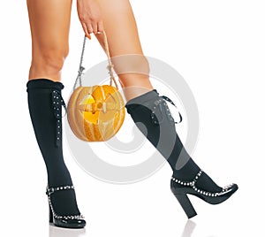 Halloween witch holding carved pumpkin near her legs.