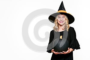 Halloween Witch holding large black pumpkin winking. Beautiful young woman in witches hat and costume holding pumpkin.