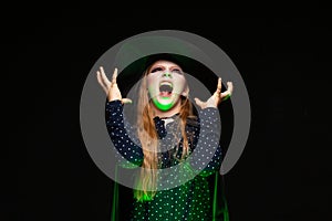 Halloween Witch over a pot of green glowing liquid conjures hands on black background. Beautiful young surprised woman