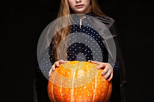 Halloween Witch with Pumpkin on black background. Beautiful young surprised woman in witches hat and costume holding