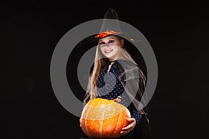Halloween Witch with Pumpkin on black background. Beautiful young surprised woman in witches hat and costume holding