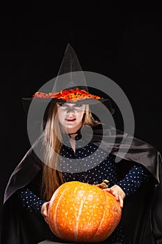 Halloween Witch with Pumpkin on black background. Beautiful young surprised woman in witches hat and costume holding