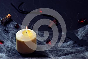 Halloween wooden cross lying next to a burning candle on a web with spiders and bats on a black background. horizontal