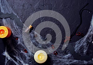 Halloween wooden cross lying next to a burning candle on a web with spiders and bats on a black background. horizontal, flat lay,