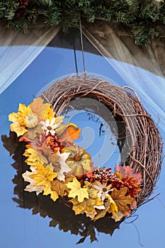 Halloween wreath with fall leaves and pumpkin hangs in a window