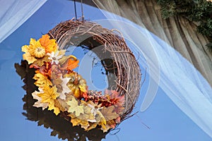 Halloween wreath with fall leaves and pumpkin hangs in a window