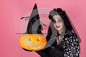 Halloween. A young woman in a costume and scary makeup with a carved Jack-o ` - Lantern pumpkin in a witch s hat