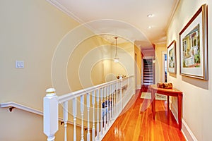 Hallway with hardwood floor and white railing to staircase.