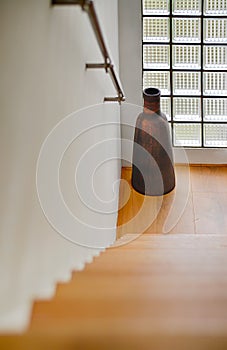 Hallway with starcase and long vase by the glass brick window