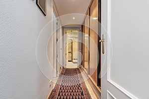A hallway with wardrobes built into one wall, access to other rooms, white wallpapered walls and a narrow rug on the floor
