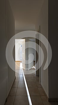 Hallway with white walls and tiles. There are open doors showing the rooms