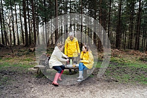 Halt for snack during hiking. Company hikers enjoying picnic on the bench, drinking hot tea, eating sandwiches in forest