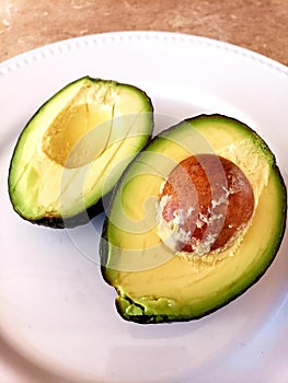 Halved avacado on a white plate with the seed pit