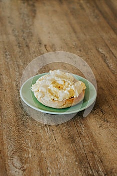 A halved bagel with poppy seeds and scrambled eggs on a green plate and light wooden table