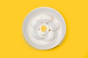 Halved boiled egg and five eggs on a white plate on a yellow background