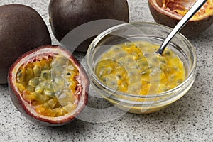 Halved fresh tropical passion fruit and a bowl with passie fruit juice and seeds close up