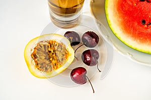 Halved passion fruit, cherry, drink and water sliced water melon on white