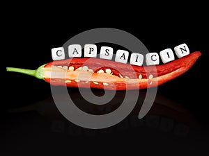 halved red hot chilli pepper with chili seed and the word capsaicin, written with white letter cubes, isolated on black photo