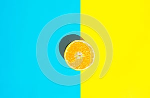 Halved Ripe Juicy Orange on Vivid Duotone Blue Yellow Background. Bright Harsh Sunlight Deep Shadow. Vibrant Neon Colors