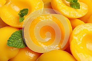 Halves of canned peaches with mint leaves as background, closeup